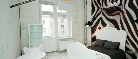 Ett rum med en vägg som har zebrasträcksmönster, en vit säng, ett vitt bord och en vit stol.
