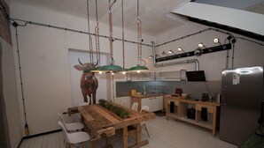A modern kitchen with a wooden dining table, white chairs, and a green pendant light. - Lofthotel Sen Pszczoły (Warsaw)