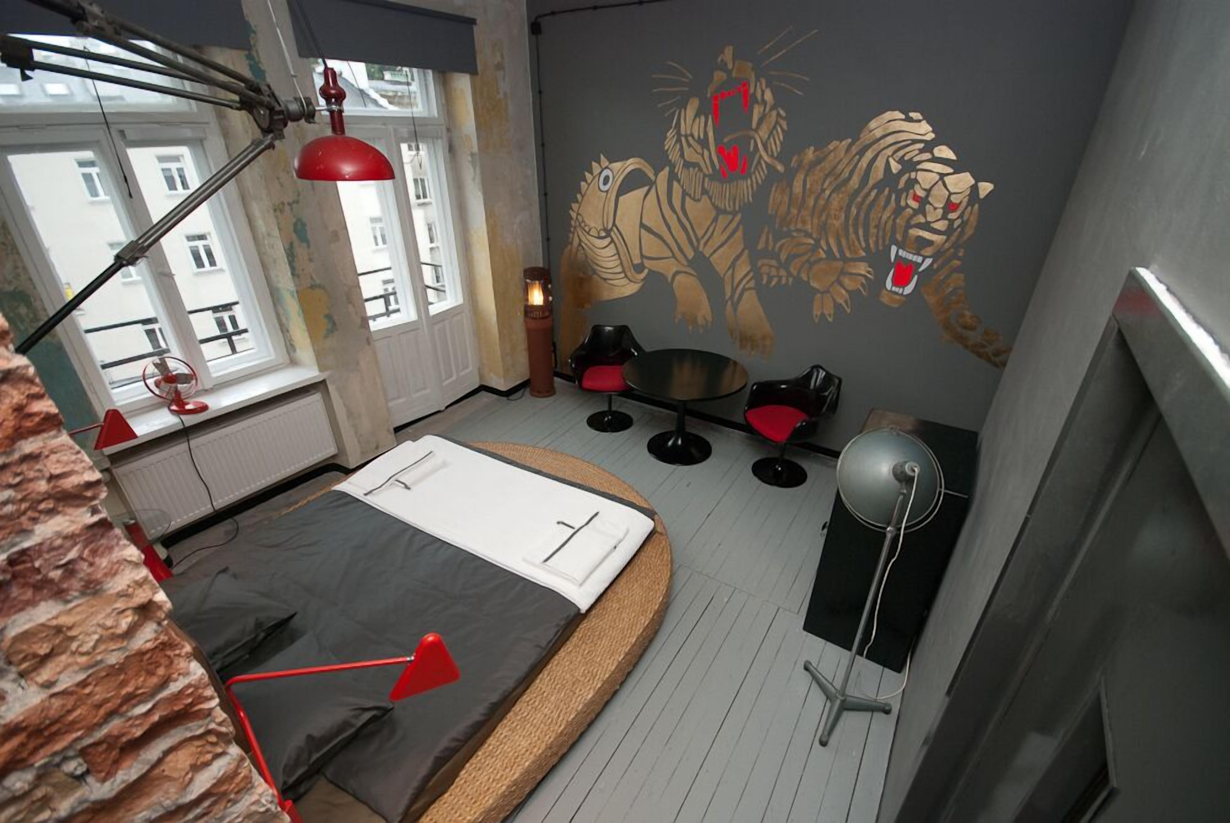 A bedroom with a bed, a red lamp, a tiger mural, and a window.