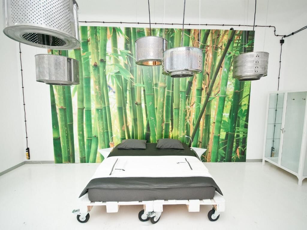 A bedroom with a bed on wheels, a large wall mural of bamboo, and hanging lights.