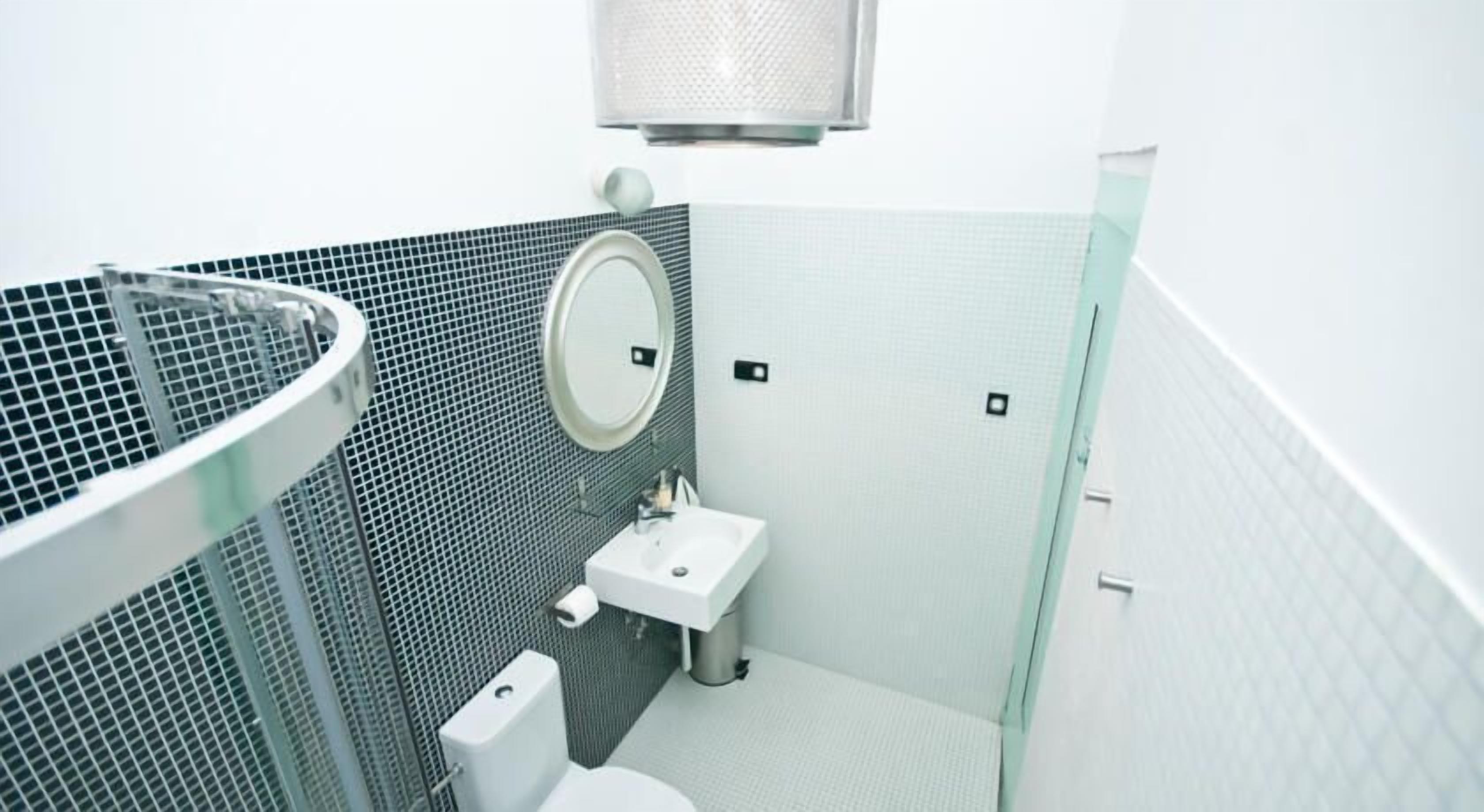 A modern bathroom with a toilet, sink, and a round mirror.