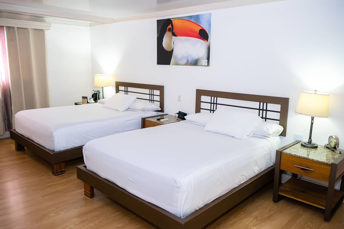 A hotel room with two single beds, wooden headboards, bedside tables with lamps, and a painting on the wall.