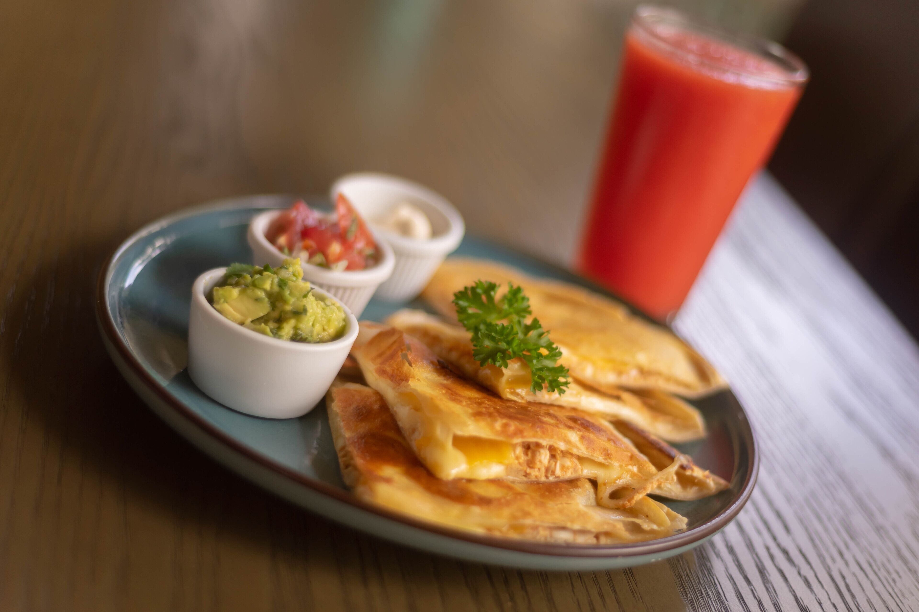 Een bord met quesadilla's, guacamole, salsa en een glas tomatensap.