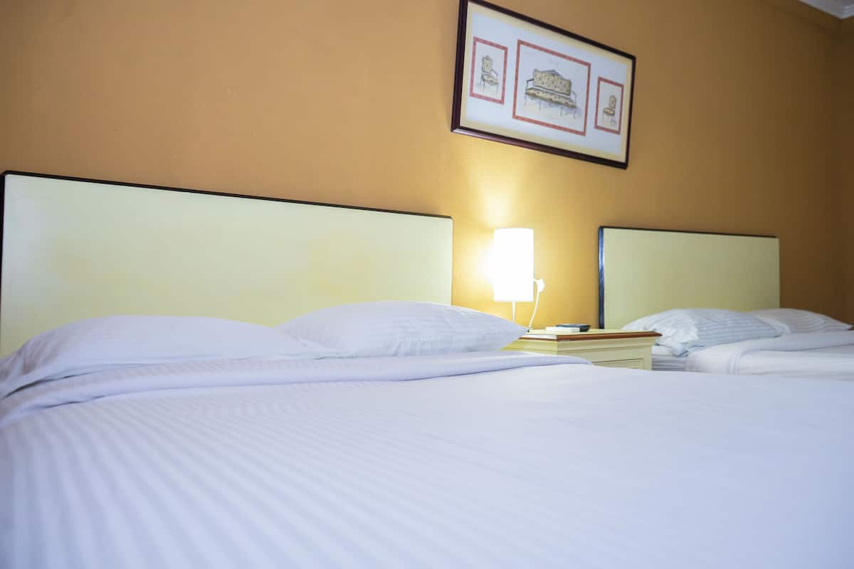 A hotel room with two beds, a bedside table with a lamp, and a framed picture on the wall.