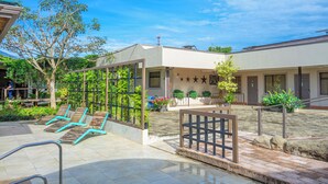 A courtyard with outdoor seating, a small garden, and a building with a tiled roof. - Hotel Zima (San Isidro de El General)
