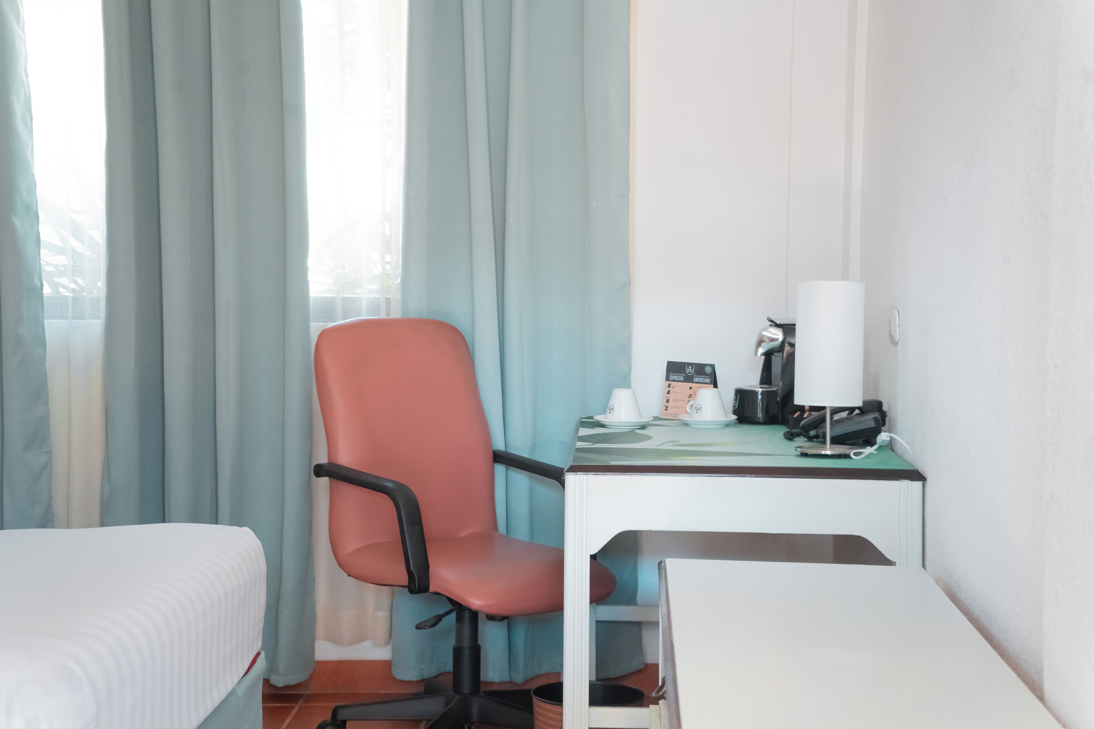 A hotel room with a bed, a desk with a chair, a lamp, and a coffee maker.