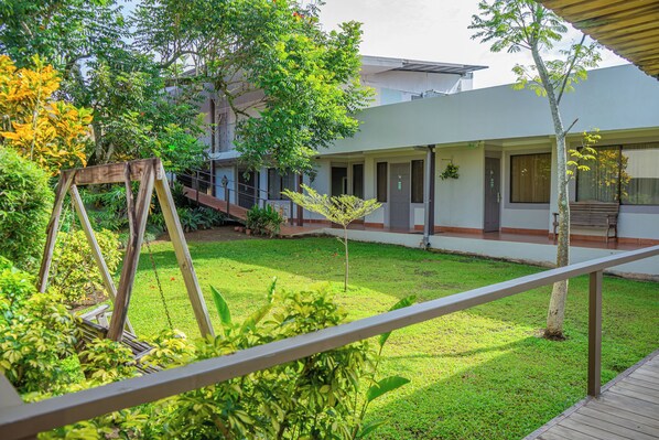 A courtyard with a swing set, a small tree, and a building with a flat roof and large windows.