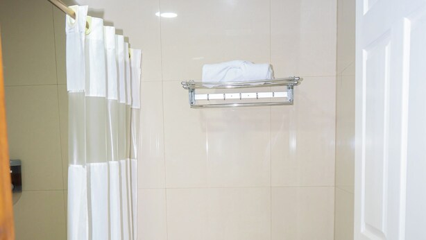 A bathroom with a toilet, a trash bin, a towel rack, and a shower curtain.