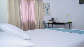 A hotel room with a bed, a desk with a lamp, a chair, and a painting on the wall.