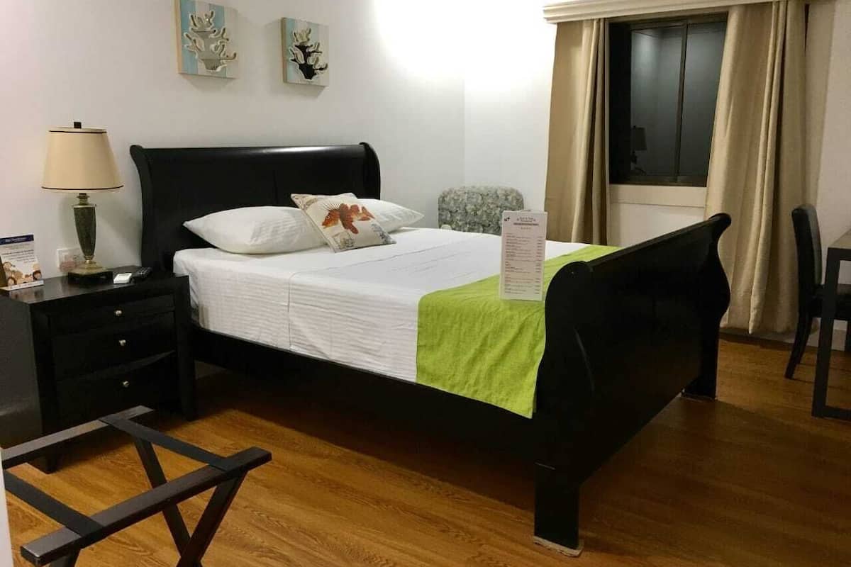 A hotel room with a bed, a nightstand, a lamp, a chair, and a window with curtains.