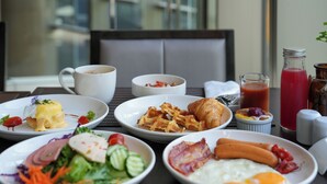 Una mesa de desayuno con diversos platos, incluyendo huevos, tocino, croissants y una ensalada.