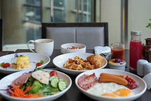 Une table de petit-déjeuner avec divers plats, notamment des œufs, du bacon, des croissants et une salade.