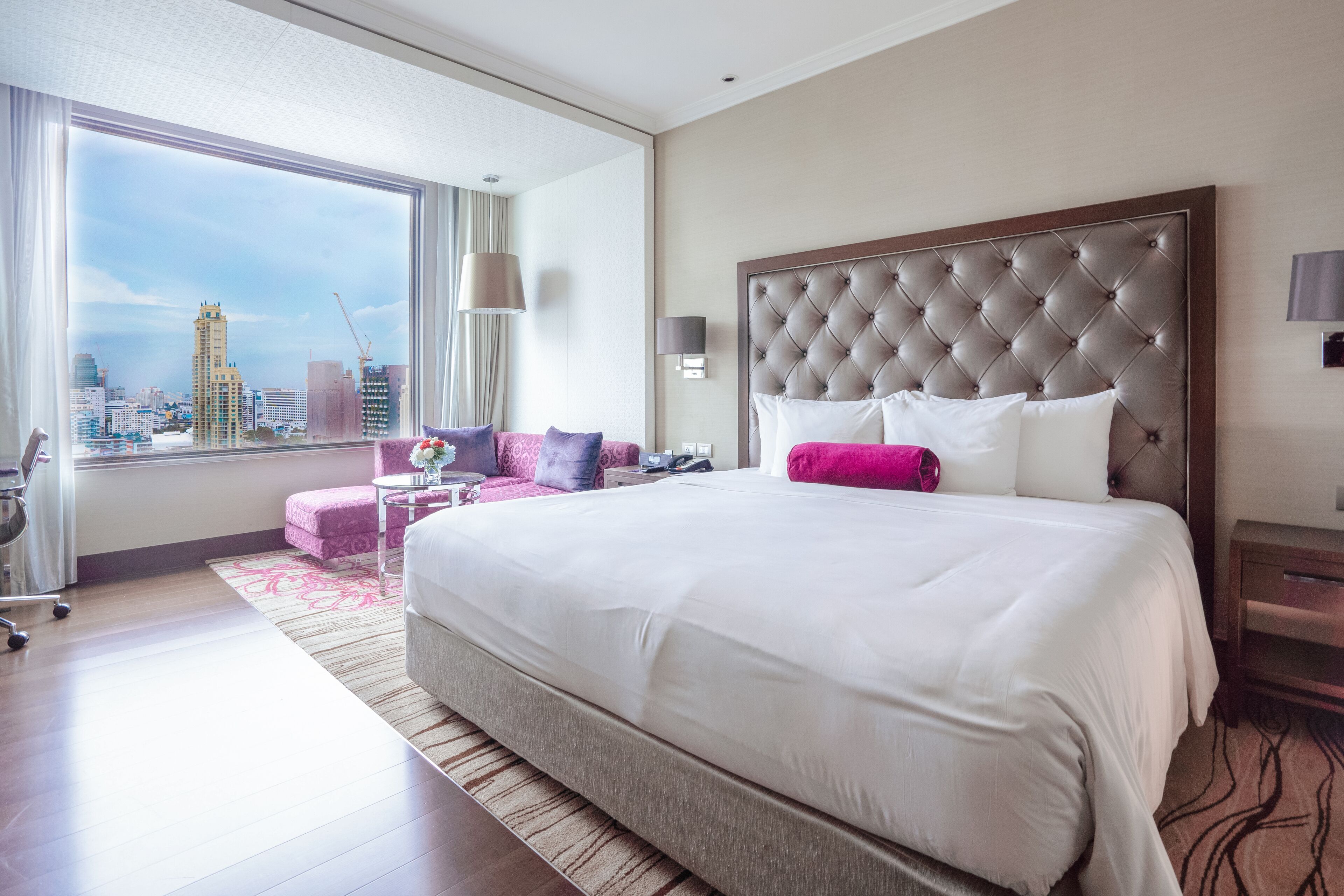 A hotel room with a large bed, a city view, a sofa, and a desk.