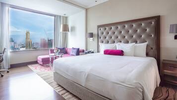 A hotel room with a large bed, a city view, a sofa, and a desk.