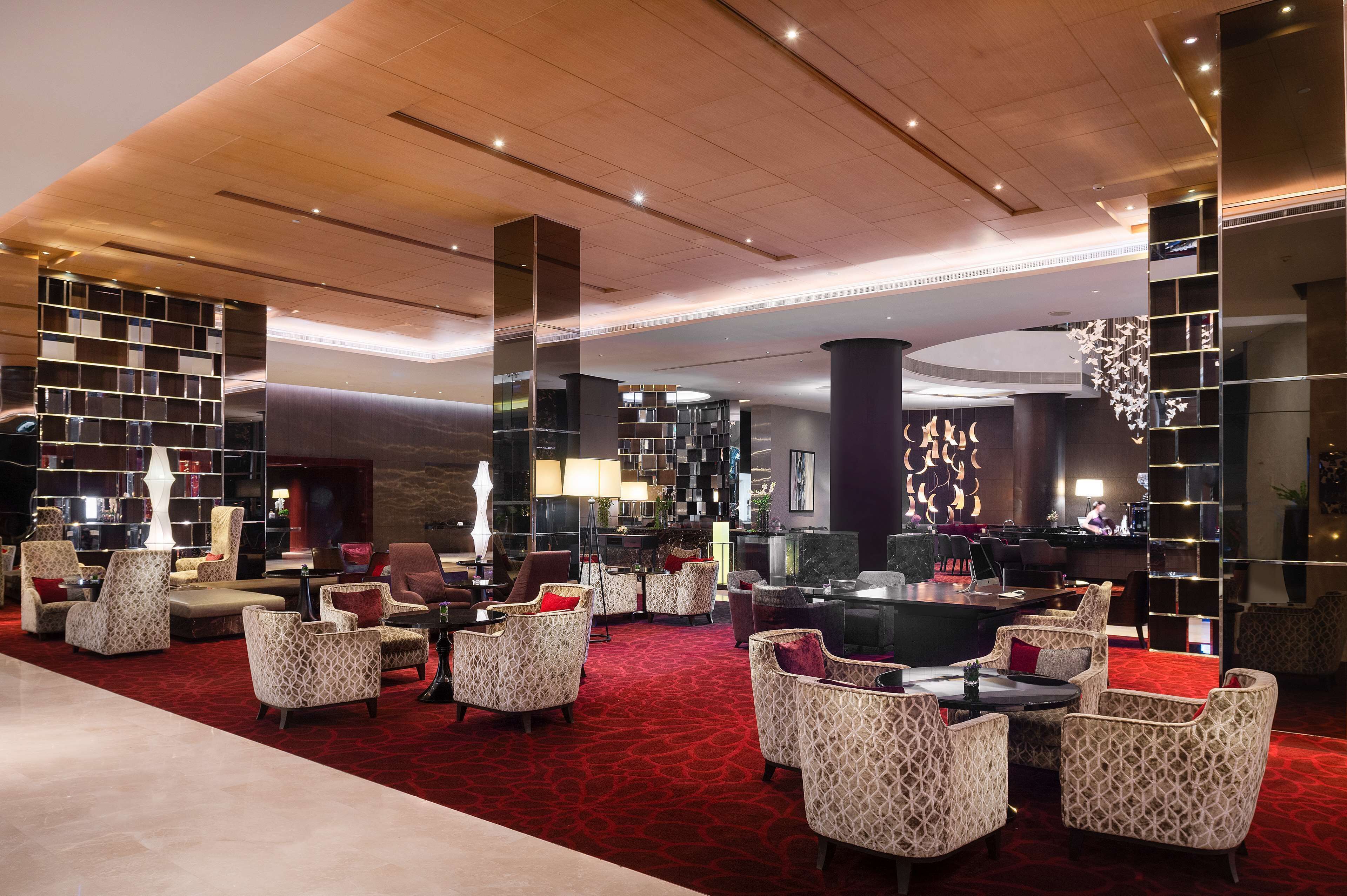 A spacious lobby with patterned armchairs, a red carpet, and a modern ceiling design.
