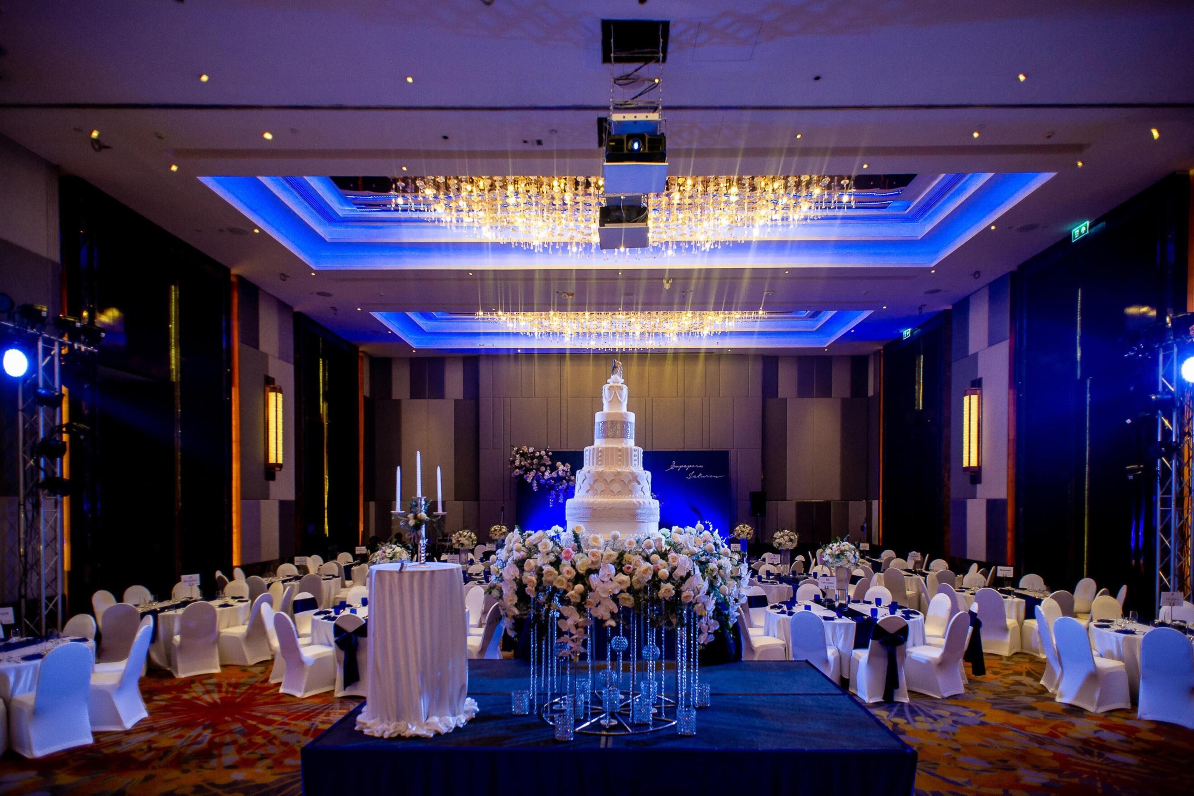 Un salón de banquetes con un pastel de bodas blanco de varios niveles, sillas blancas y candelabros.
