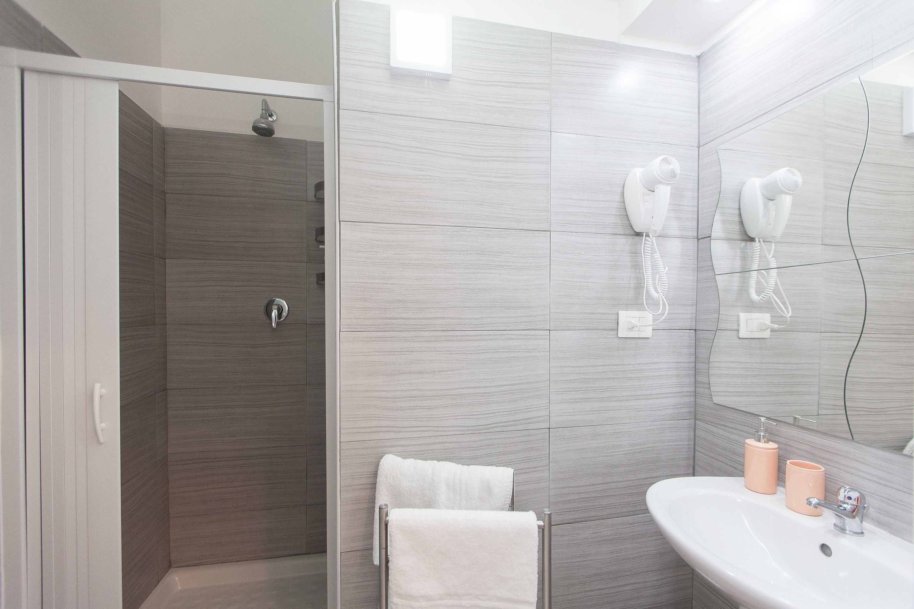 A modern bathroom with a shower, a sink, and two hair dryers mounted on the wall.