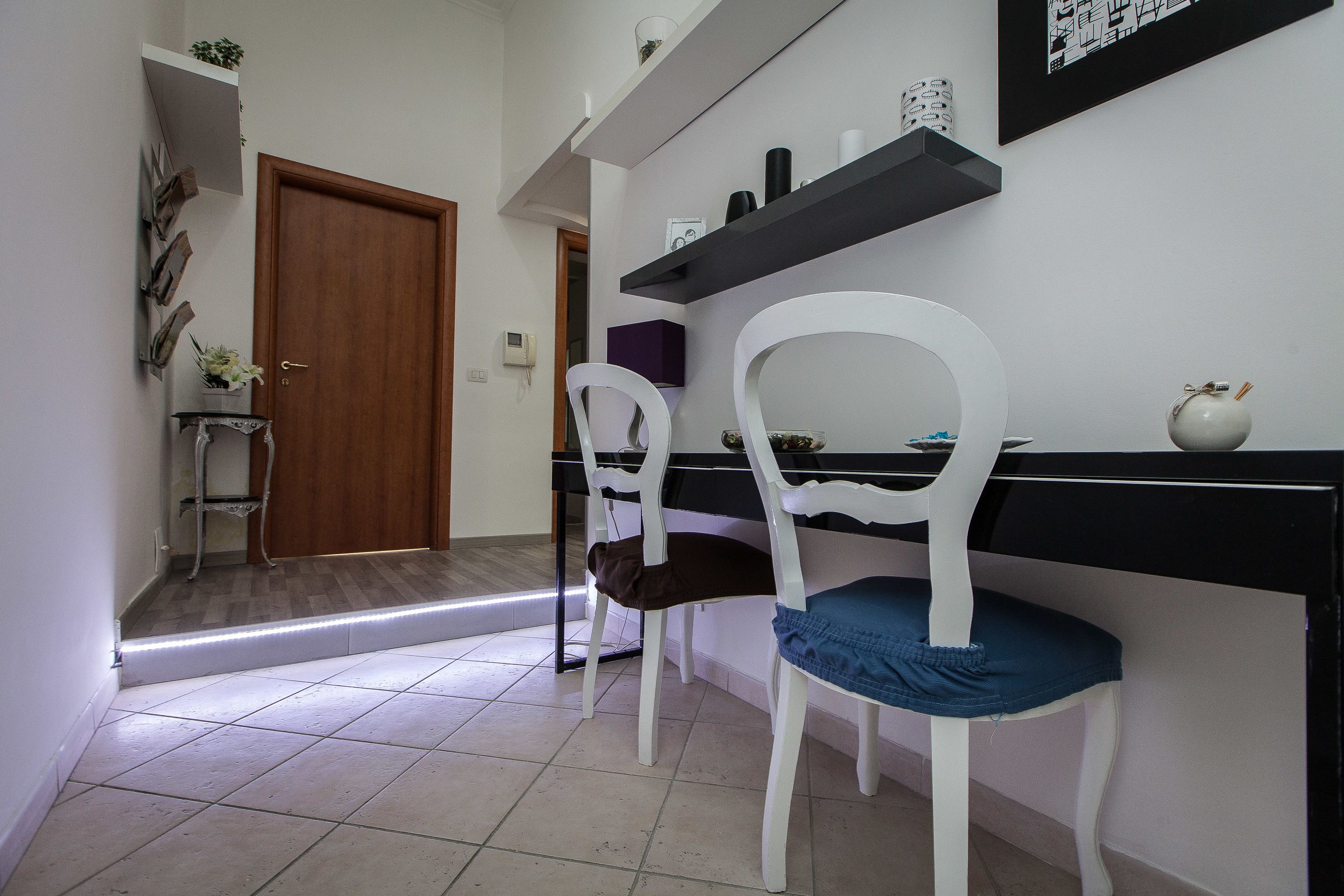 A hallway with a wooden door, white chairs, a black table, and shelves with decorative items.