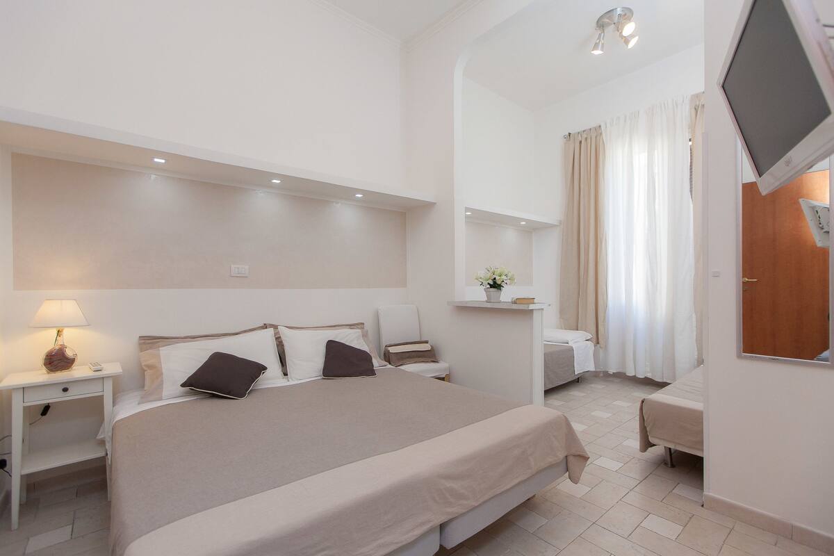 A hotel room with a large bed, bedside tables, a desk, and a TV.