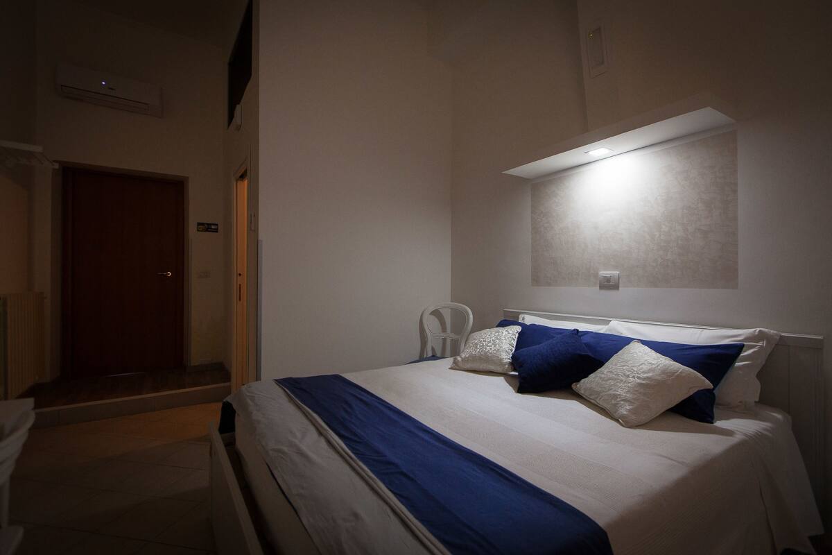 A hotel room with a bed, a chair, a desk, and a door.