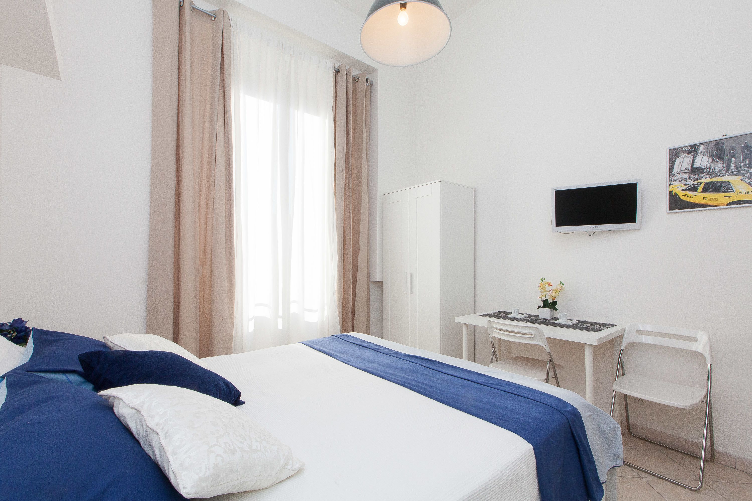 A hotel room with a bed, a desk, a chair, a TV, and a wardrobe.