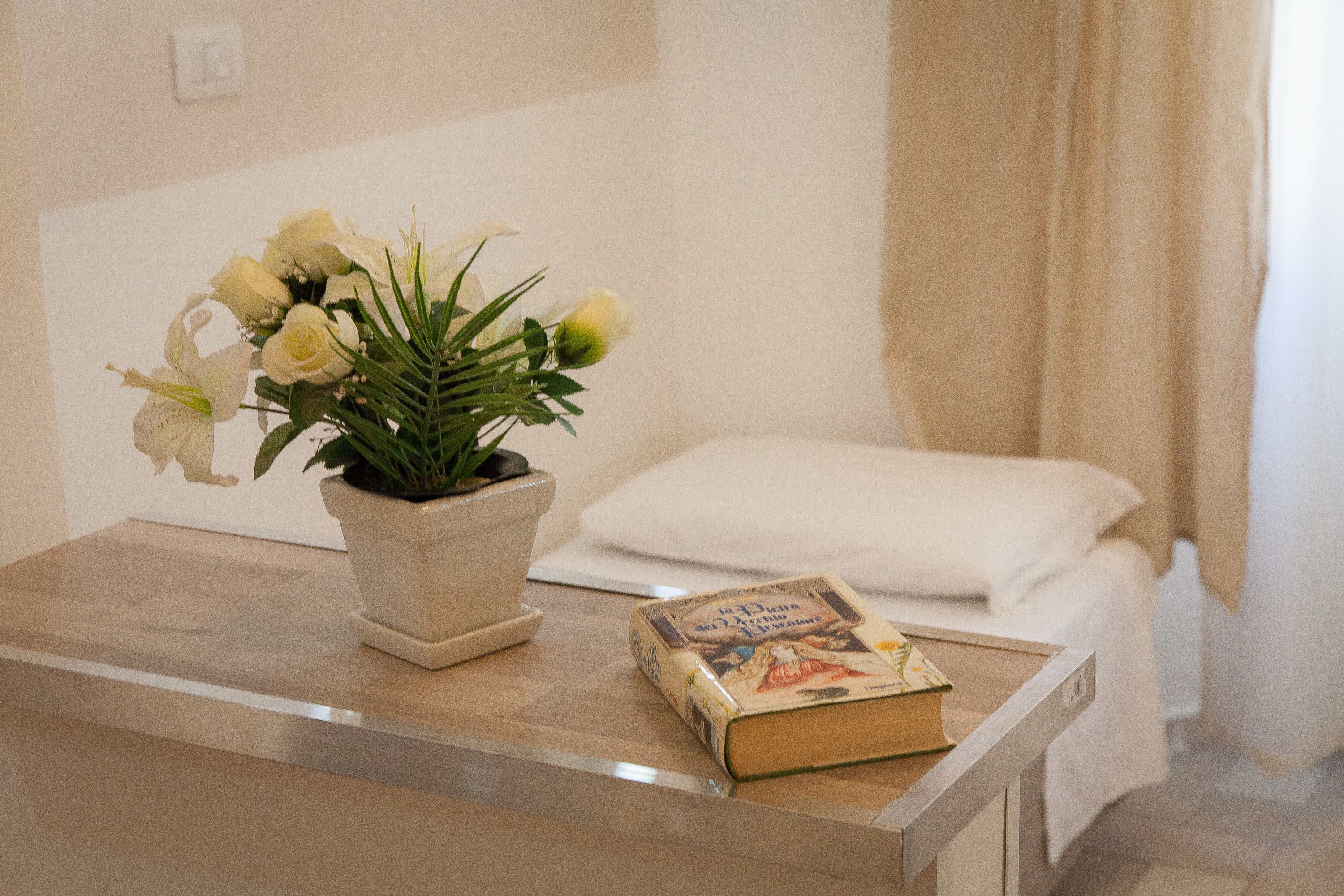 Ein Zimmer mit einem Bett, einem Nachttisch mit einem Buch und einer Zimmerpflanze.