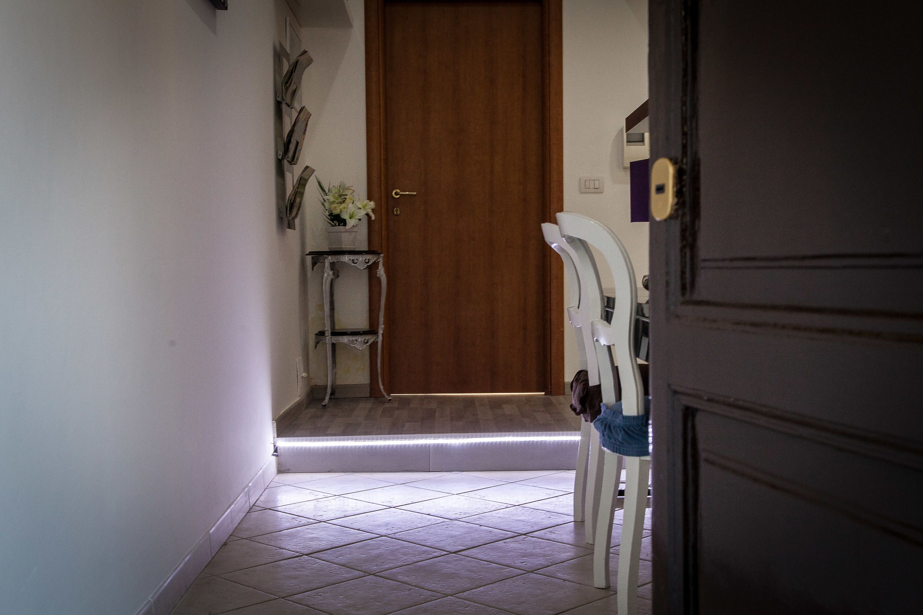 A hallway with a wooden door, a white chair, and a small table with a vase of flowers.