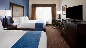 A hotel room with two beds, a desk, a television, and a dresser.