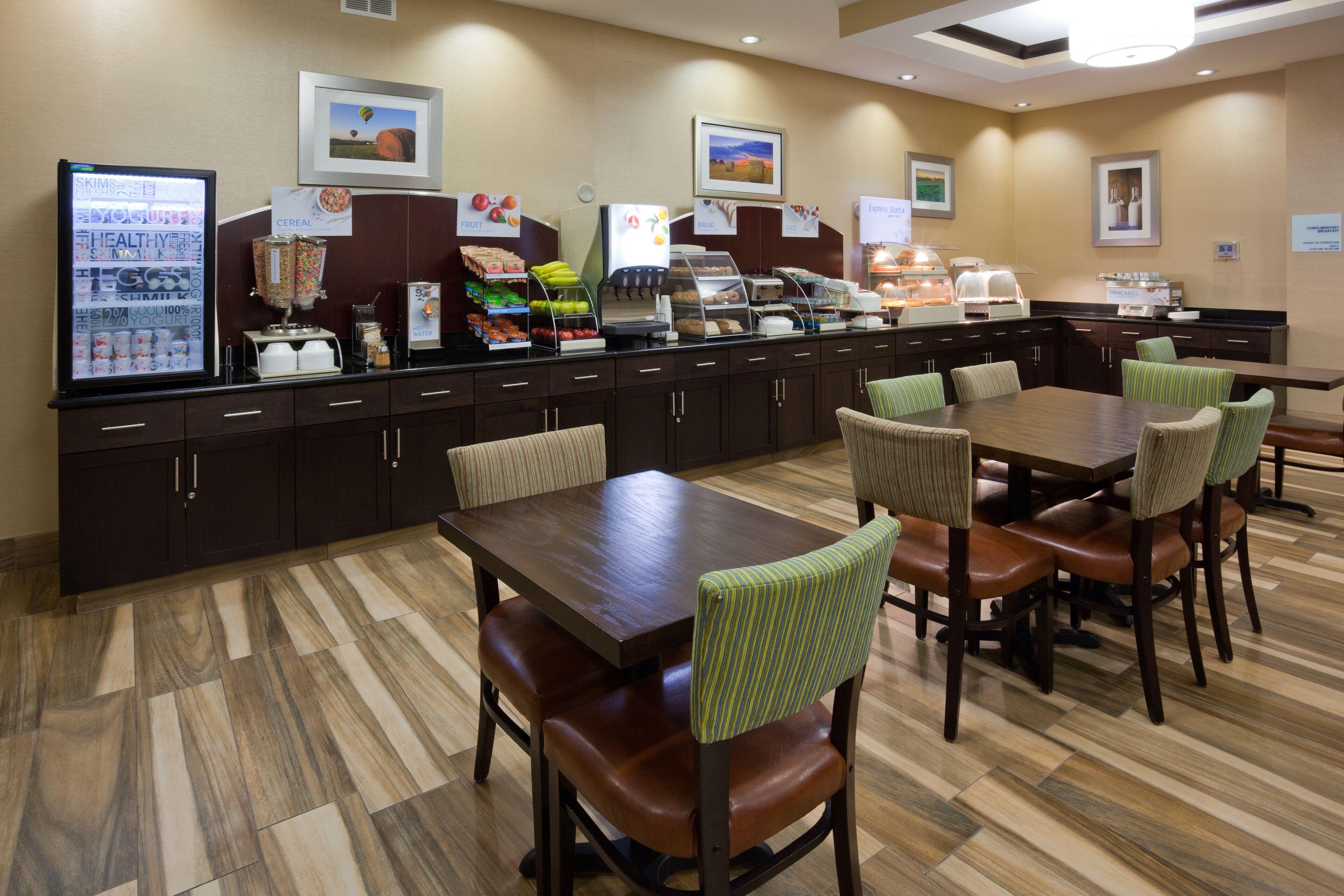 A breakfast area with a refrigerator, coffee machine, and various food items. There are tables and chairs for dining.