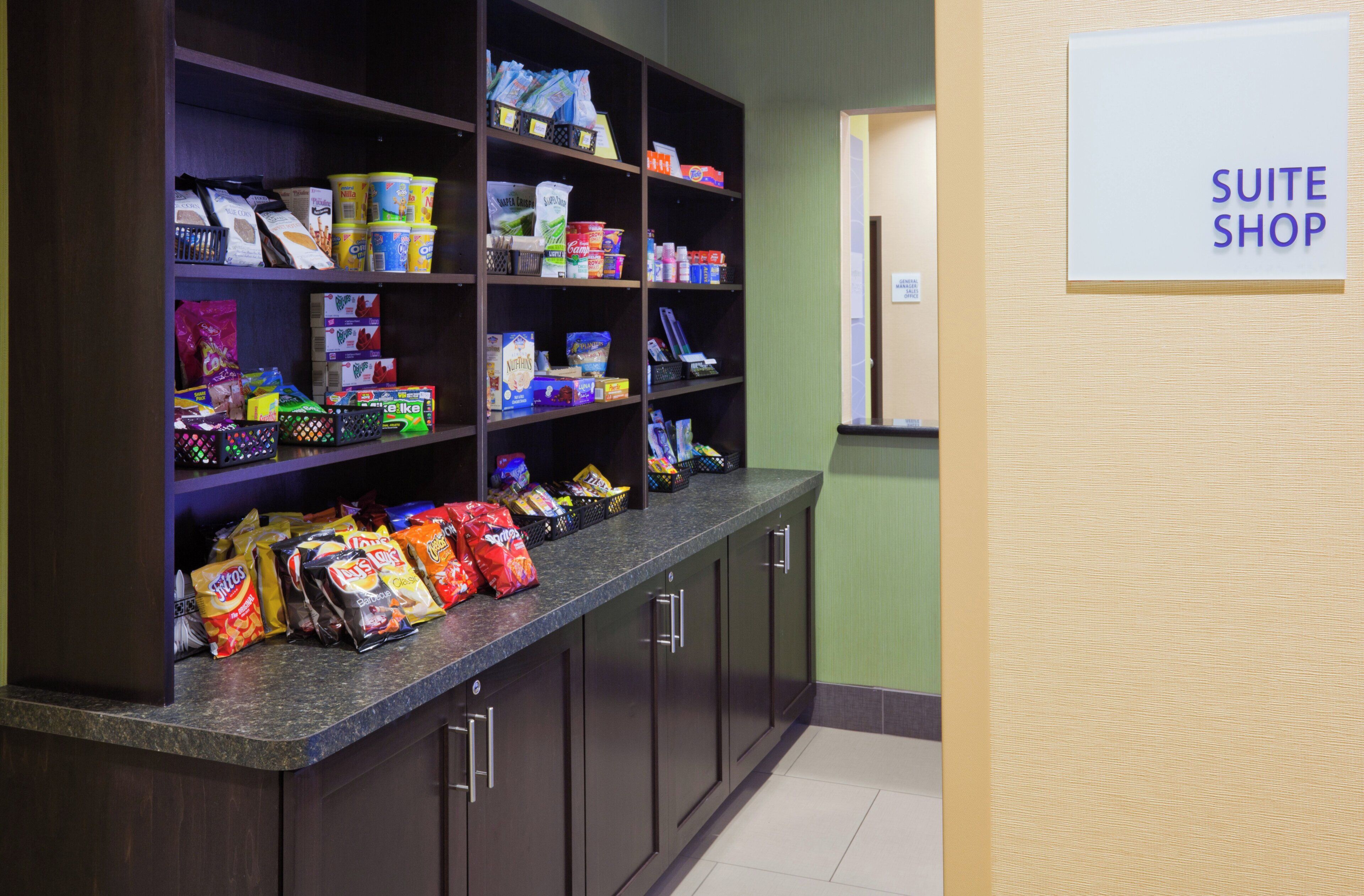 A kitchenette area with shelves stocked with snacks and beverages, a countertop with bags of chips, and a sign indicating a 'SUITE SHOP'.