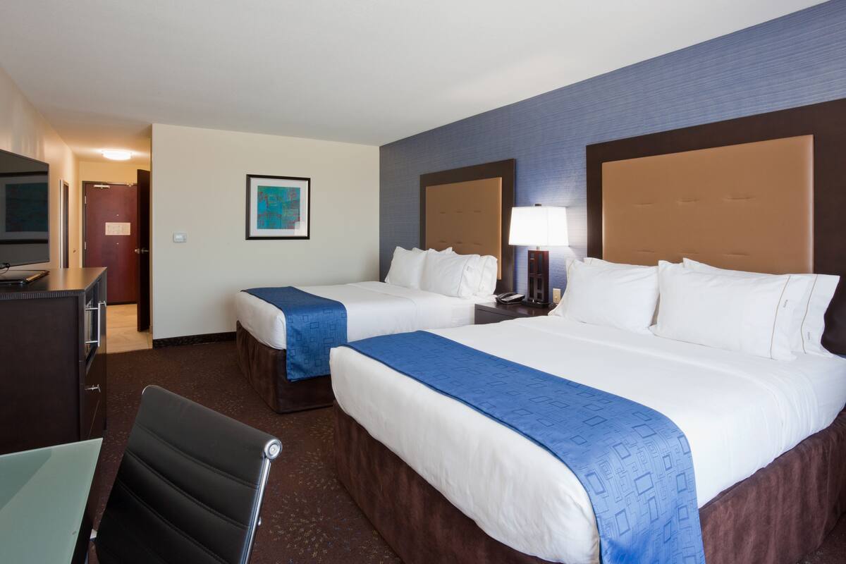 A hotel room with two beds, a desk, a chair, a TV, and a framed picture on the wall.
