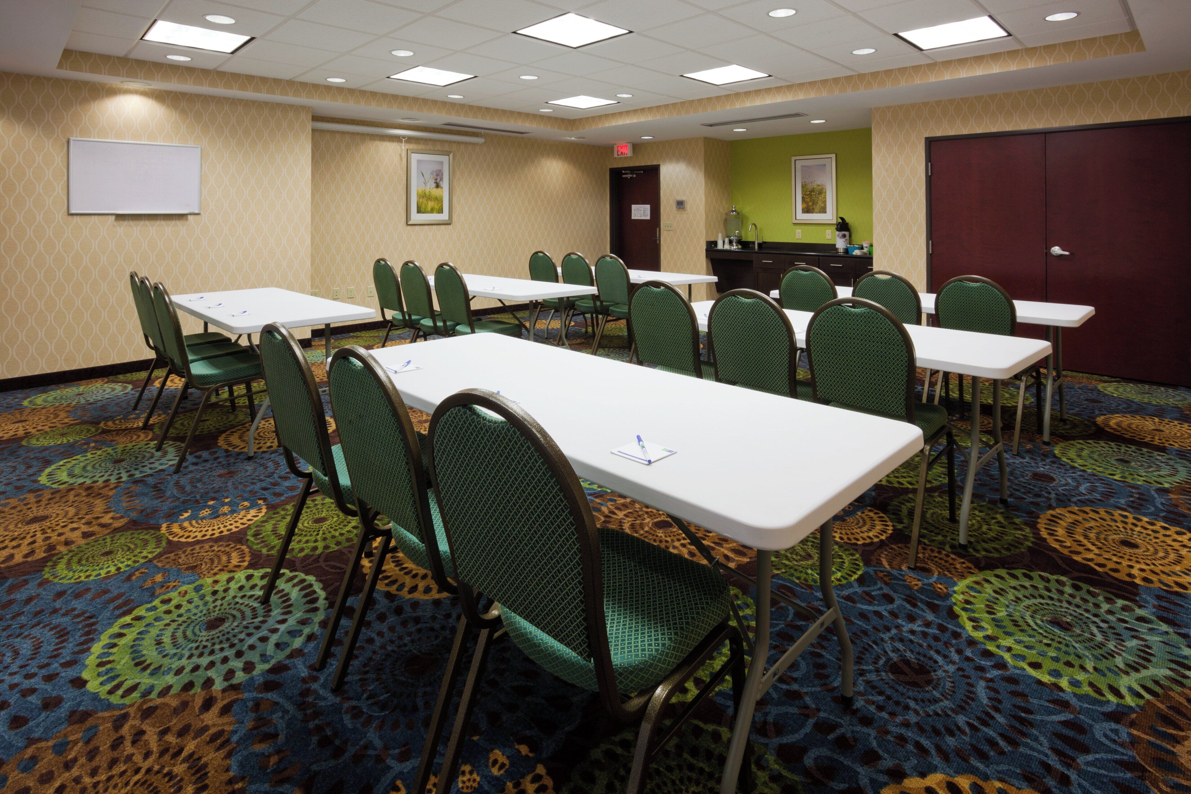Un salón de conferencias con varias mesas y sillas, una kitchenette y una puerta.