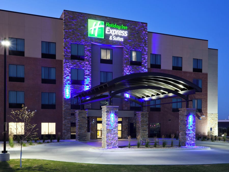 A Holiday Inn Express & Suites hotel with a modern architectural design, featuring a prominent illuminated sign and a covered entrance area.