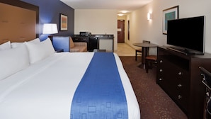 A hotel room with a large bed, a desk with a computer, a television, and a dining area.