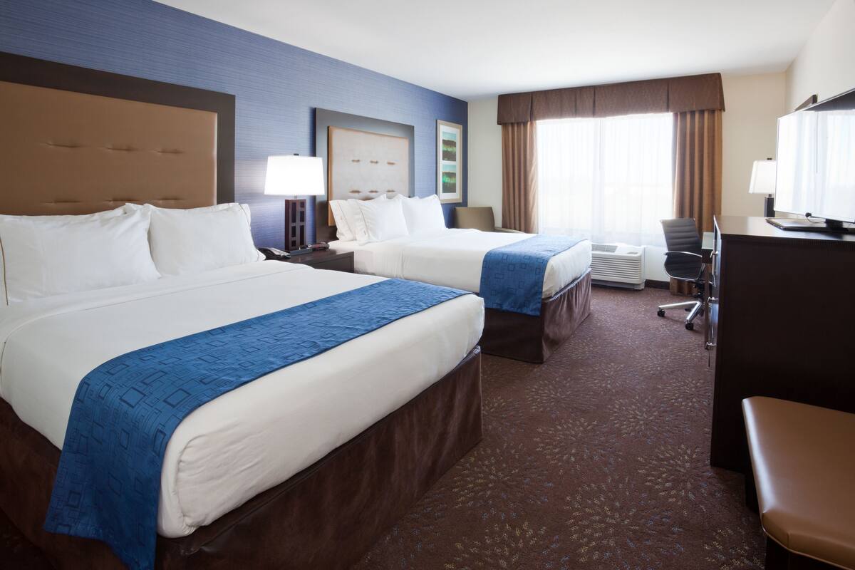 A hotel room with two beds, a desk, a chair, and a television.