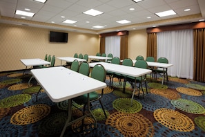 A conference room with multiple tables and chairs, a flat-screen TV mounted on the wall, and patterned carpet. - Holiday Inn Express Hotel & Suites Fort Dodge by IHG (Fort Dodge)