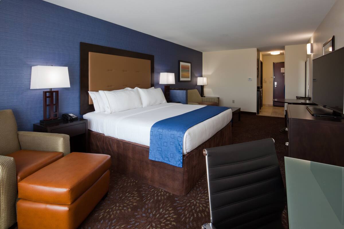A hotel room with a large bed, two bedside tables with lamps, a desk with a chair, and a television.
