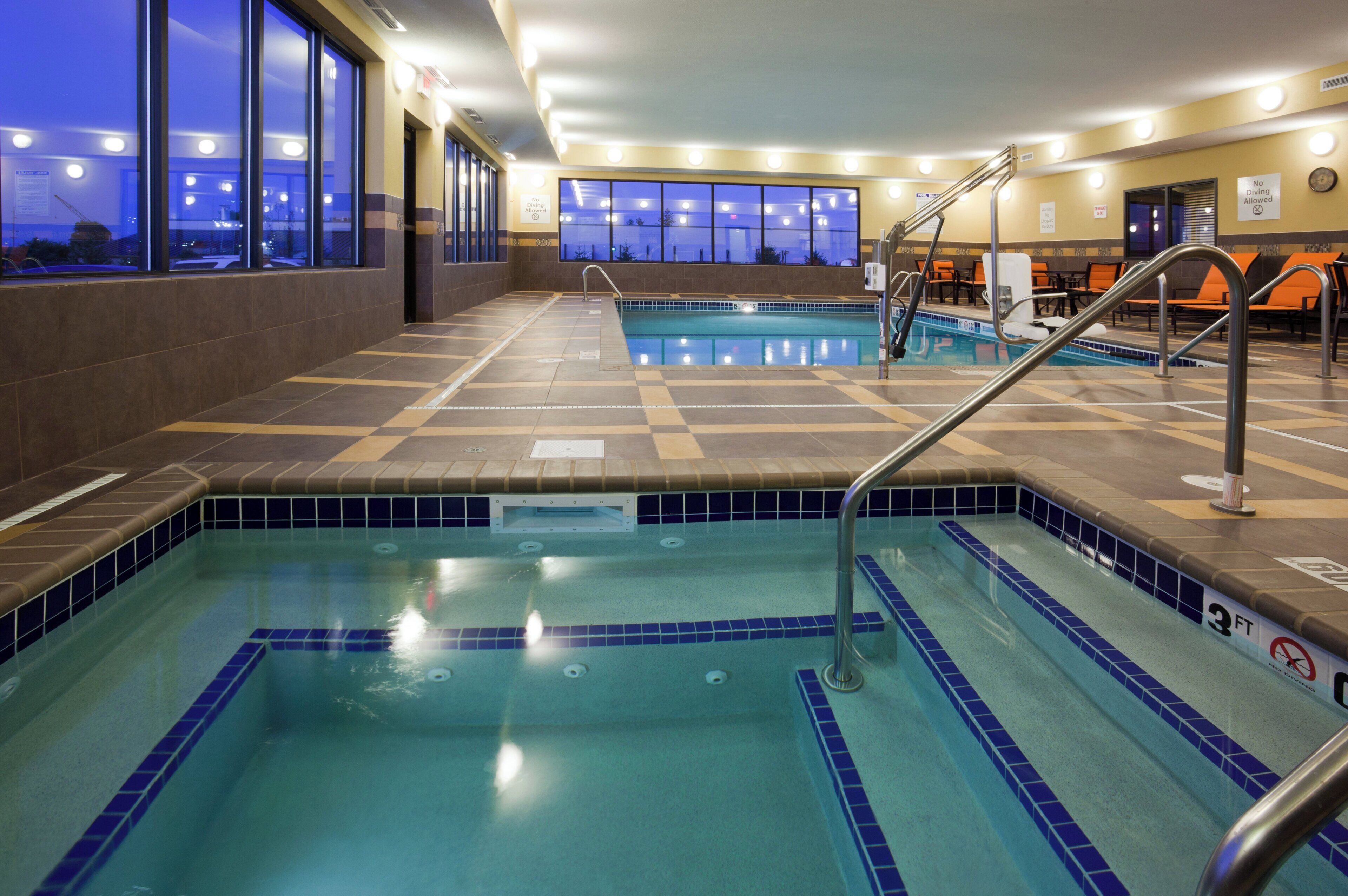 An indoor swimming pool with clear water, tiled flooring, and a view of the night sky through large windows.