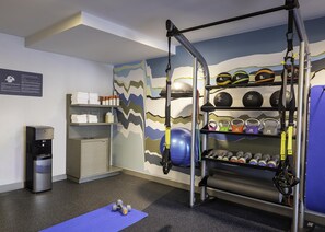 Ein Fitnessraum mit Klimmzugstange, Kettlebells, Kurzhanteln und Wasserspender.