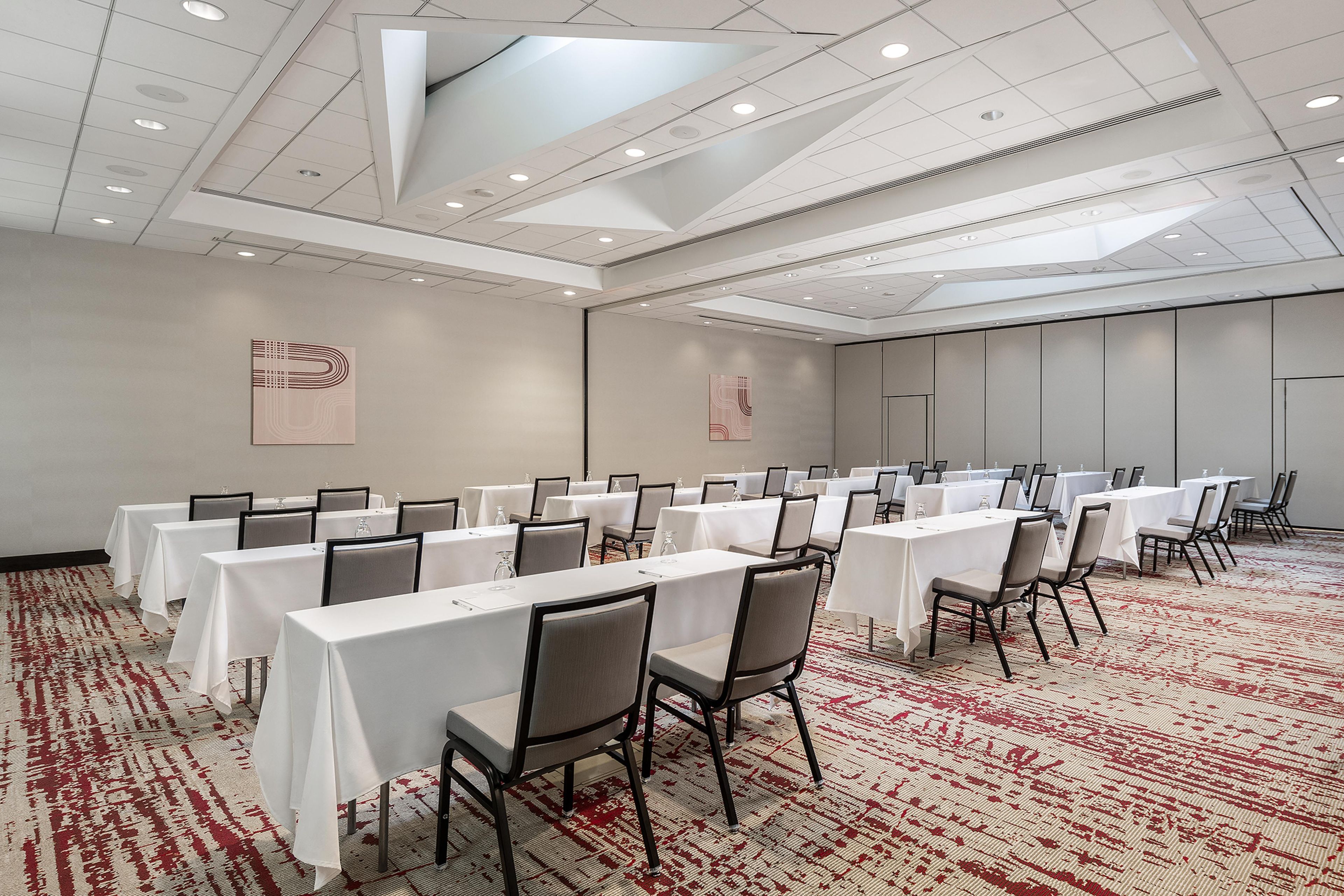 A conference room with tables and chairs, a patterned carpet, and a ceiling with recessed lighting.