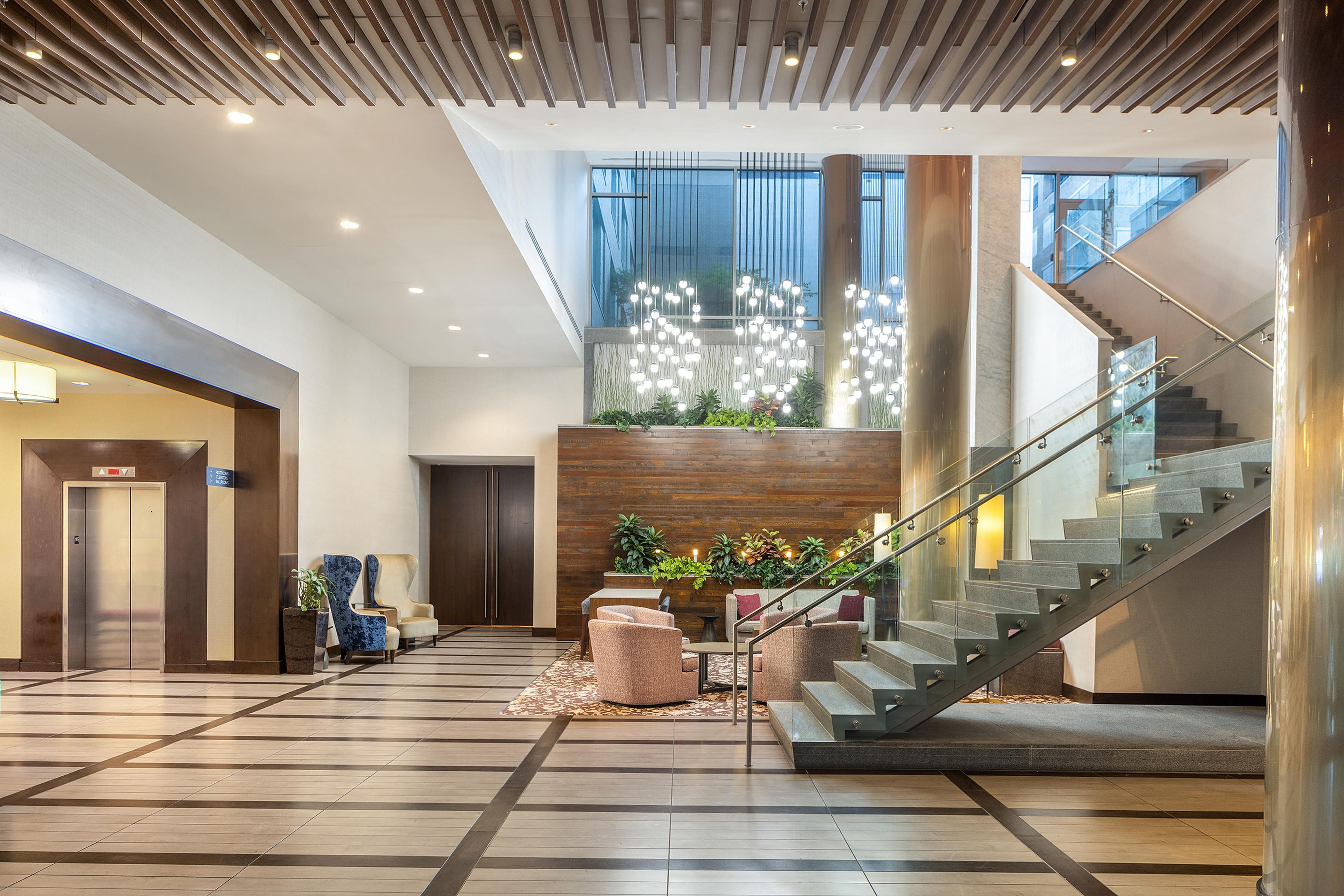 A spacious lobby with a modern staircase, a reception desk, and a seating area with plants.