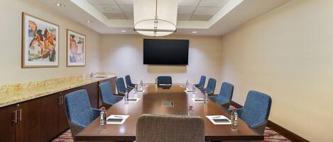 A conference room with a long table, blue chairs, a flat-screen TV, and artwork on the walls.
