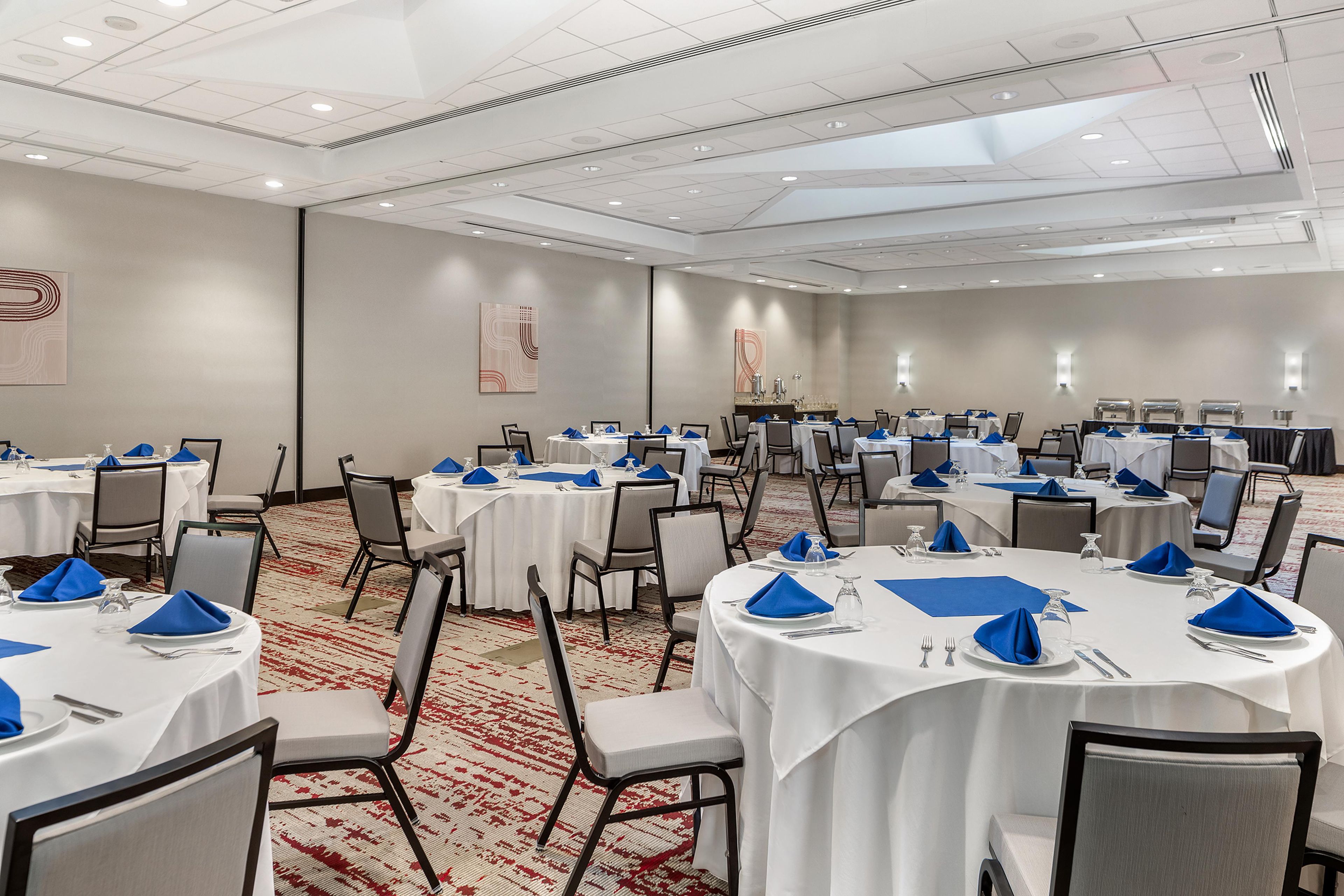 A conference room with multiple round tables, each set with white tablecloths, blue napkins, and silverware.