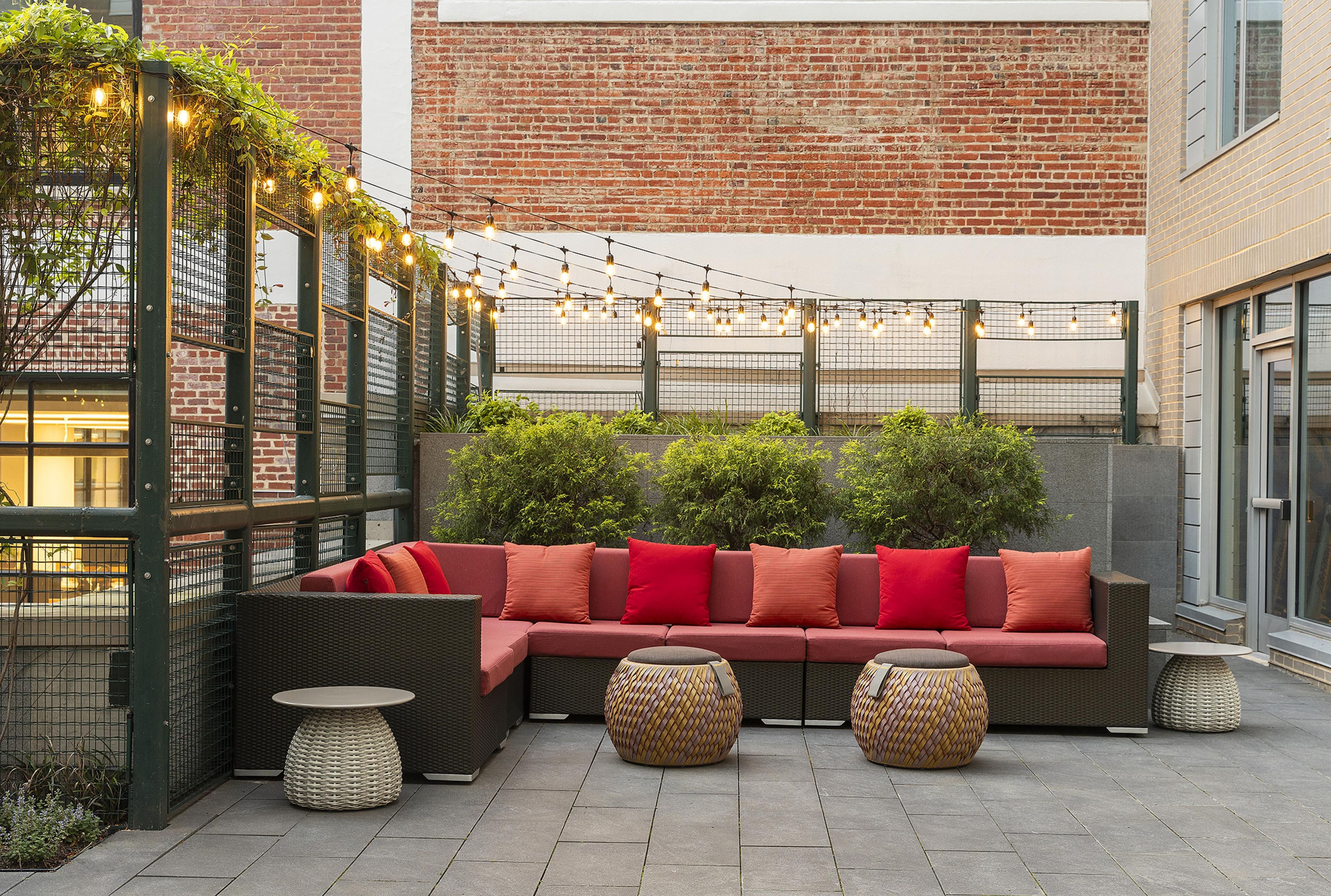 An outdoor seating area with a red sofa, wicker tables, and string lights.