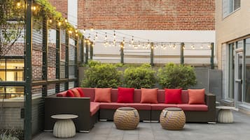 An outdoor seating area with a red sofa, wicker tables, and string lights.