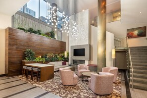 Eine moderne Lobby mit einer Sitzecke, einer Wand aus Holz mit Pflanzen, einem Flachbildfernseher und einer Treppe.