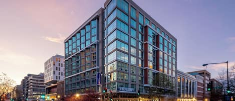 A modern hotel with a glass facade, located at a city intersection.
