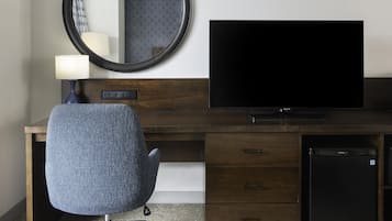 A hotel room with a wooden desk, a television, a chair, a mirror, and a small refrigerator.