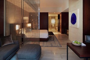 A modern hotel room with a large bed, a sofa, a dining table with a bowl of fruit, and a view of the city through a glass wall. - Park Hyatt New York (New York)