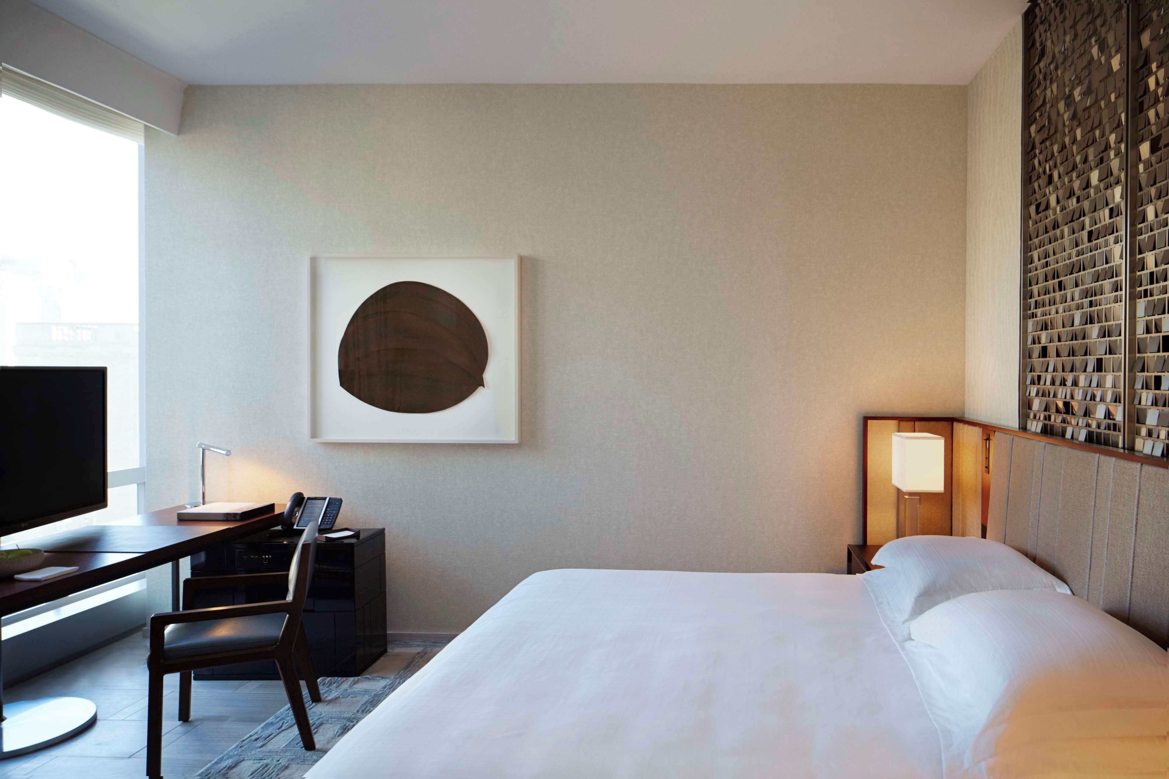 Una habitación de hotel con cama, escritorio, silla y un cuadro abstracto grande en la pared.